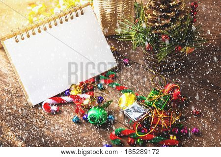 Merry christmas and Happynew year text on blank notebook with snow gift box daisy flower candy ball and cane pine decoration on vintage wooden background.
