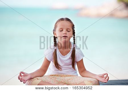 Child doing meditating exercise on wooden platform sea shore outdoors. Healthy lifestyle. Yoga girl