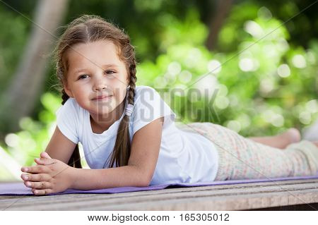 Child doing meditating exercise on wooden platform sea shore outdoors. Healthy lifestyle. Yoga girl