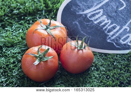closeup of three red tomato with grass background and black sign