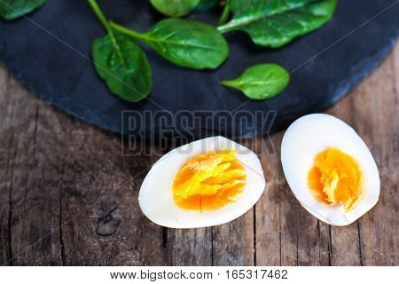 Salad with green spinach baby leaves and boiled eggs cut in a half on rustic wooden table.