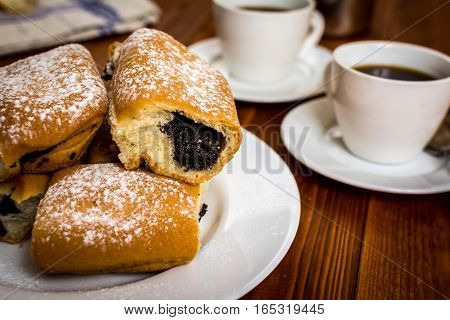 Baked sweet buns with poppy and coffee on wood table