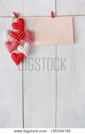 Valentine background with sewed pillow diy handmade hearts and empty greeting card on red clothespins at rustic white wood planks. Happy lovers day mockup, copy space, vertical