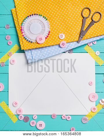 Sewing thread - buttons scissors fabric and empty tag on turquoise wooden background. Selective focus. Scrapbboking. Flat lay. Place for text. Vertical image.