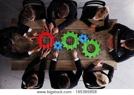 Group of business people seen from above gathering cogs of business sitting together around the table