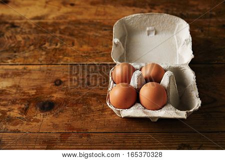 Presentation of opened recyclable egg carton for six eggs containing four big ecological eggs on a rough rustic brown wooden table