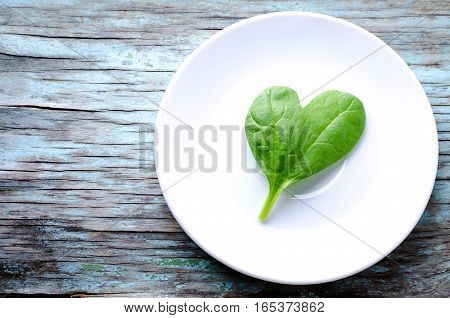 Fresh Baby spinach heart shape leaf on white plate, blue wooden background. Top view with copy space. Love, Healthy, Ecology concept, horizontal
