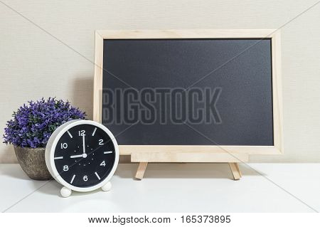 Closeup alarm clock for decorate show 9 o'clock with wood black board on white wood desk and cream wallpaper textured background selective focus at the clock