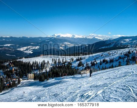 View from the high to the ski resort which attracts skiers on the ski slopes the snow-capped mountain peaks snowy trail a steep ski