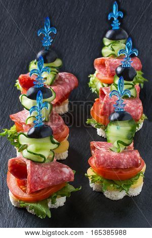 Colorful canape on skewers with vegetables and sausage on a slate plate. Tasty appetizer for a party or banquet. Selective focus vertical