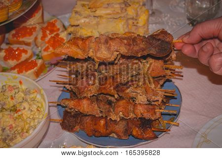 grilled meat kebabs on the holiday table bread and red caviar in the background hand takes a skewer with shashlik
