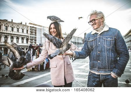 Couple in Saint Mark Square Venice playing with local pigeons - Tourists having fun in Venezia