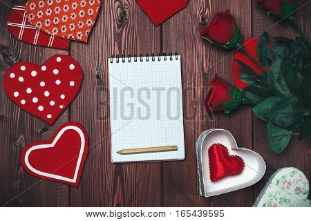 Opened mock up notepad, toy hearts and red roses on wooden table. Romantic template. Valentines day concept. Toned image, top view.