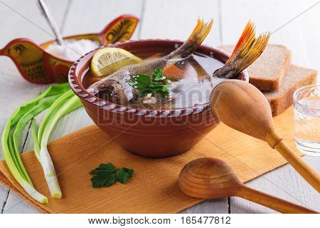 Traditional Russian fish soup in a clay bowl on a wooden table. Rustic style