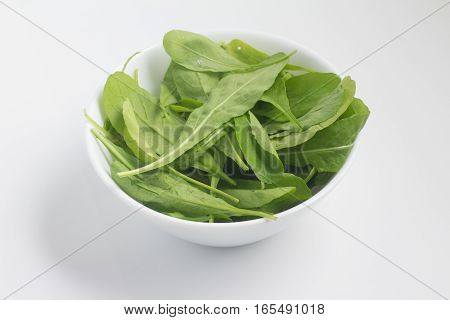 Arugula Leaves into a bowl over a white background