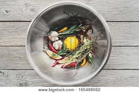 Cooking background. Lemon, herbs, chili, garlic and other seasoning ingredients in metal bowl on rustic wood, top view. Vegetables and herbs ready for making steak marinade