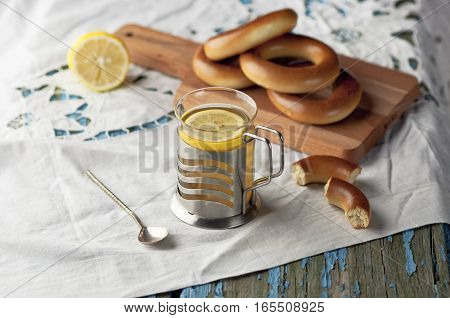 Mug of tea with lemon and bagels on a wooden background. Tea with lemon Baking bagels white tablecloth.