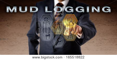 Oil industry manager in suit touching MUD LOGGING on an interactive virtual computer monitor. Petroleum industry technology concept for downhole drilling mud examination during the drilling process.