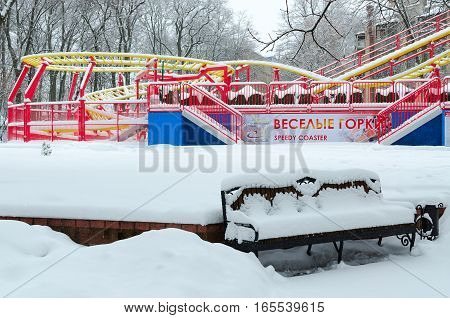 GOMEL BELARUS - JANUARY 12 2017: Snowy attraction "Funny roller coaster" and bench in winter park during snowfall Gomel Belarus