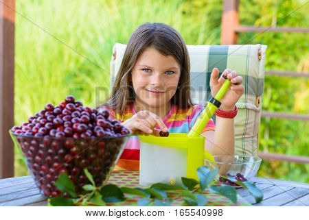 stoning fresh cherries by young pretty girl in the garden - using cherry pitter