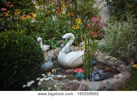 Decorative plastic flowers swans and ducks in the artificial garden pond.