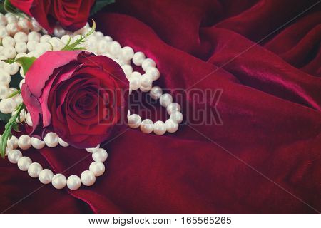fresh red rose with pearls on scarlet velvet background, retro toned