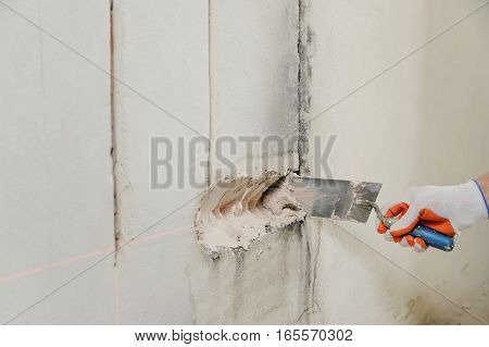 Installing electrical socket box. A worker puts plaster into the hole on the wall to install socket box.