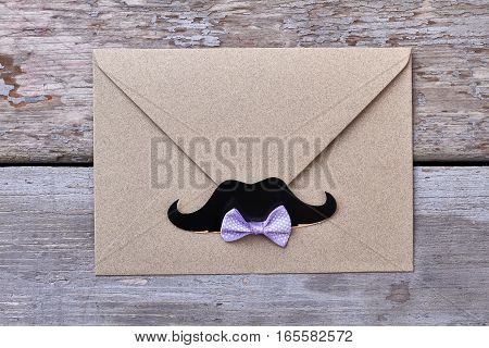 Envelope with mustache on wood. Spotted bow tie on paper. Waiting for a letter.