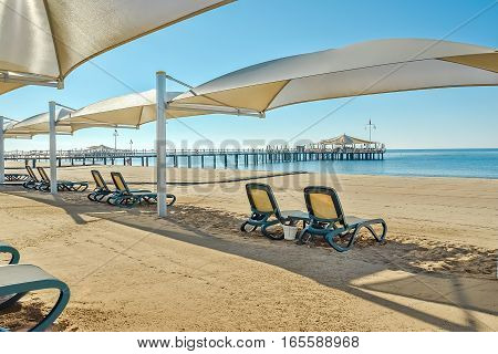 Sandy beach with sun loungers and parasols on the seafront in sunny summer day. Foreground blurred