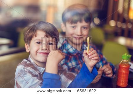 Happy little boys eating french fries in fast food restaurant