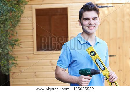 Handyman Standing Outside Garden Shed With Tools