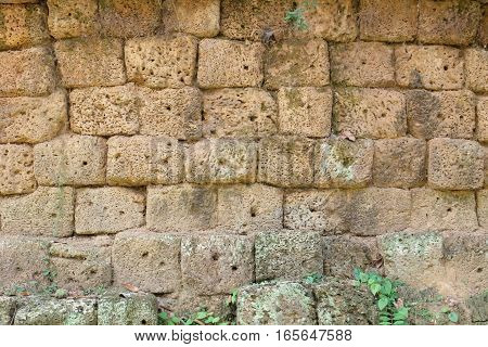 A wall made of volcano stone blocks. Each cube is rectangle or square with an irregular shape and porous surface. This ancient wall is part of the overgrown and long lost ruins of the sunken city Angkor in Cambodia.