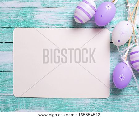 Easter or spring background. Decorative violet eggs and empty tag on turquoise wooden background. Selective focus. Place for text.