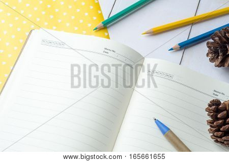 Blank daily planner notebook with pen and color pencils on white wooden background