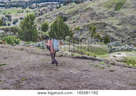 QUILOTOA, ECUADOR, FEBRAURY - 2016 - Andean worker carrying a bag while walking to dirty path at border of Quilotoa crater Latacunga Ecuador