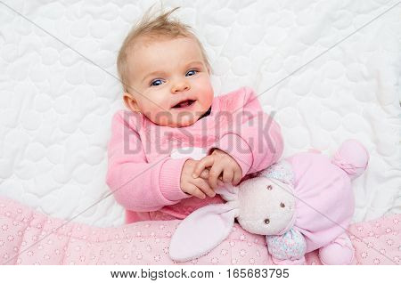 Happy Infant Baby Girl Smiling On Bed With His Toy Bunny