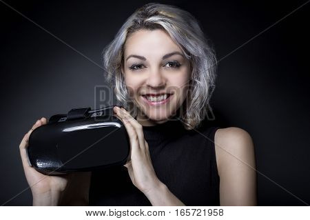 Woman holding a virtual reality headset used in VR movies or video games. The gadget is wearable technology for leisure. She is advertising the non branded generic device.