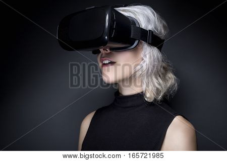 Woman wearing a futuristic looking virtual reality headset goggles. The device is technology that lets video gamers experience VR or AR augmented reality