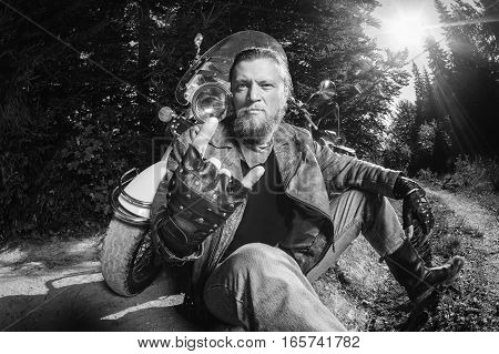 Unshaven Male Biker Sitting On Dirt Road Near Motorcycle