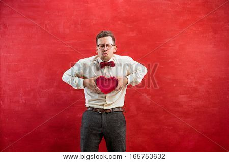 Young beautiful man with abstract heart on red studio background