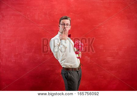 Young beautiful man with flowers on red studio background