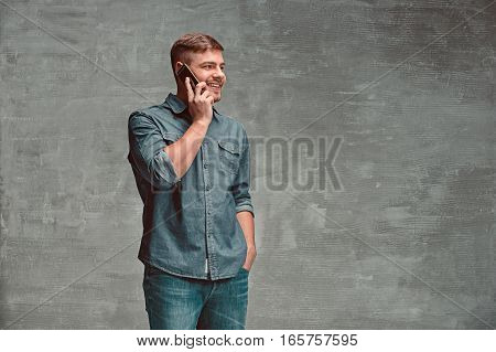 The young smiling caucasian businessman on gray studio background talking on cell phone