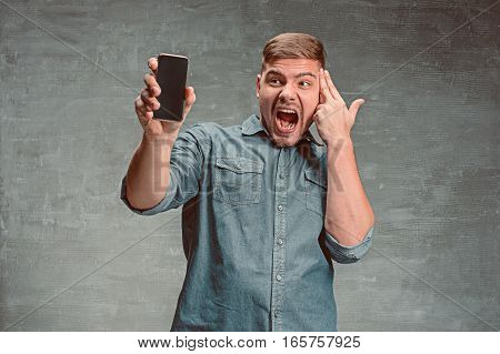 The young smiling caucasian businessman on gray studio background with mobile phone