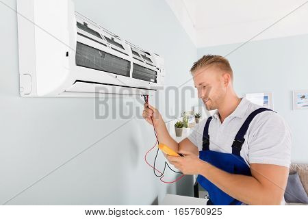 Male Electrician Checking Air Conditioner With Digital Multimeter