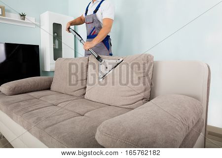 Young Male Worker Cleaning Sofa With Vacuum Cleaner