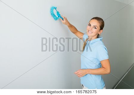 Young Woman Cleaning The Ceiling With Mop On The Corridor Of The Building