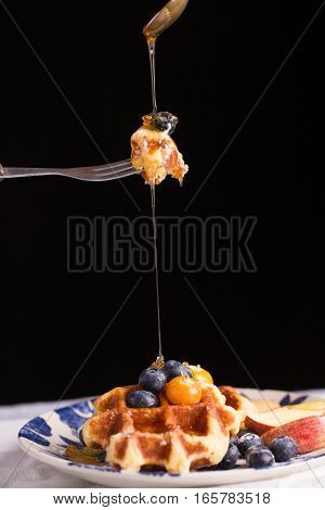Blueberry waffle set in a nice dish and a fork cut in piece with pouring honey on black background copy space.