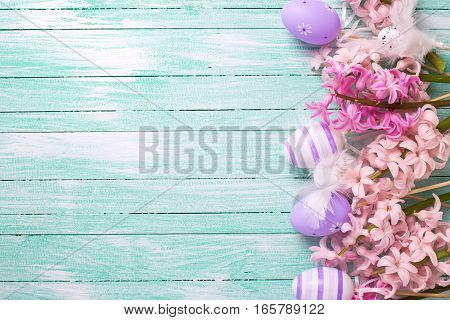 Easter or spring background. Border from decorative violet eggs and pink hyacinths flowers on turquoise wooden background. Selective focus. Place for text.