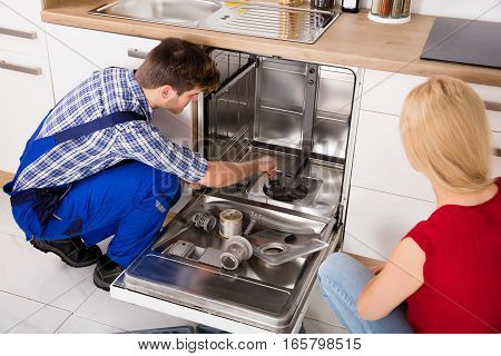 Young Woman Looking At Repairman Repairing Dishwasher In Kitchen