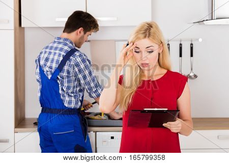 Young Frustrated Woman Looking At Huge Bill From Plumber Standing In Kitchen